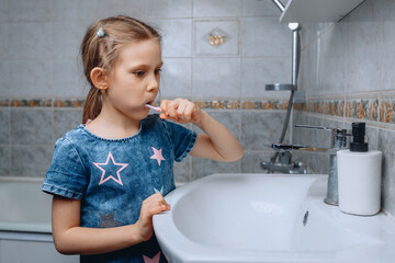 A little girl observes oral hygiene and thoroughly cleans her teeth in the bathroom next to the sink.