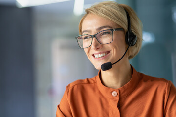 Close-up photo. Portrait of a young woman student in a headset, glasses and an orange shirt looking...
