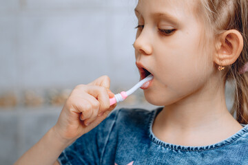 An approximate face of a child of a girl doing a daily dental hygiene procedure on a blurry background in the bathroom.