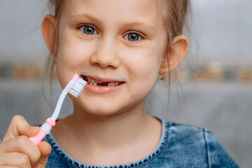 Funny little girl 6 years old close-up holding a pink toothbrush smiling. Blurred tile background in the bathroom.