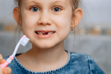 A little beautiful girl with a cheerful face in close-up holds a toothbrush on a blurry tile background.