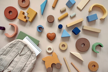 top view close-up wooden children's toys in pastel colors, a backpack with a notepad and a textbook book and a wooden heart in the center