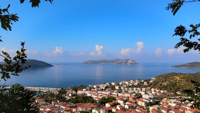 Drone flying between trees towards the view of Kaş and Meis Island (Kastellorizo) in Antalya, Turkey, revealing the Mediterranean coastal landscape and turquoise waters.