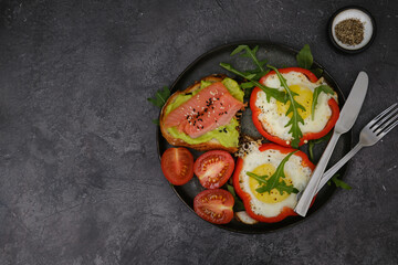 Breakfast plate with fried eggs, red pepper, salmon sandwiche and avocado on black background.