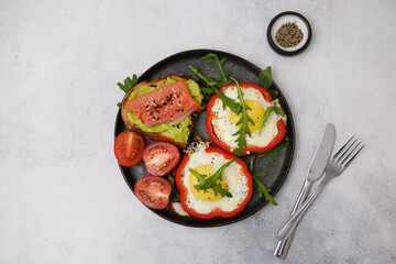 Breakfast plate with fried eggs, red pepper, salmon sandwiche and avocado on grey background.