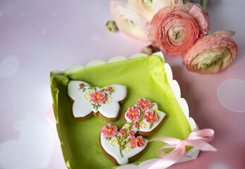 Handmade gingerbread butterfly and tulip in gift box next to bouquet of ranunculus asiaticus flowers on pink background. Beautiful gifts for Mother's day, March 8, birthday, Valentine's day. Postcard