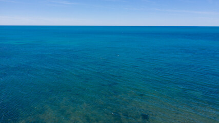 Aerial view of the blue waters of the Mediterranean Sea and specifically of the Tyrrhenian Sea from Sardinia. Sunlight is reflected on the surface of the water. Sky is on background.
