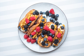 Fresh sweet rolls with cream cheese and fresh blueberries, strawberries, raspberries and currants on a white plate on a white-grey stripped surface. Copyspace. Bakery advertisement. Food advertisement