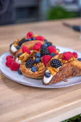 The freshly baked, large brown sweet rolls with cream cheese and fresh blueberries, strawberries, raspberries and currants on a white plate on wooden table