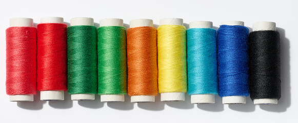 Multicolored spools of sewing threads on a white background, top view