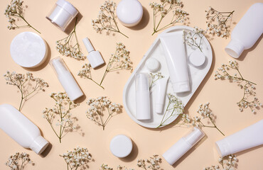 White plastic tubes, jars, and gypsophila branches on a beige background, containers for cosmetic...