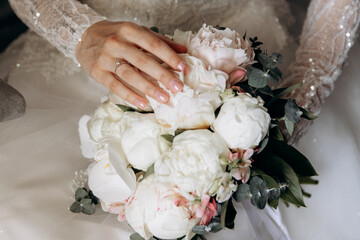 a young girl in a white wedding dress holds a bouquet of flowers and greenery with a ribbon in her hands. a bouquet of flowers piona