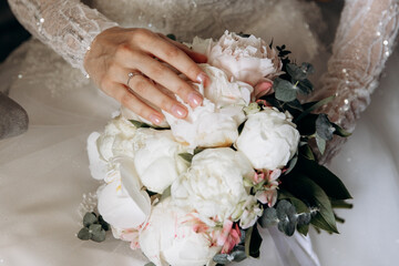 a young girl in a white wedding dress holds a bouquet of flowers and greenery with a ribbon in her hands. a bouquet of flowers piona