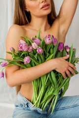 Portrait of sexy beautiful young woman with long hair. Model with a bouquet of lilac tulips on white. Spring. Holidays.