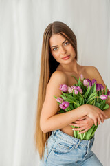 Portrait of sexy beautiful young woman with long hair. Model with a bouquet of lilac tulips on white. Spring. Holidays.