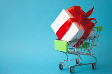 A gift box in a shopping basket on a blue background. The concept of online shopping. Online shopping and delivery. Holiday gifts.