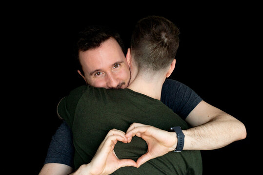 Young Gay Couple Making A Heart Shape With His Hands Isolated On Black Background.