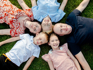 A happy large family lies on the floor in a park on a green lawn in a circle of connected heads. Shooting from above