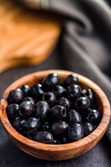 Pitted black olives in wooden bowl on kitchen table.