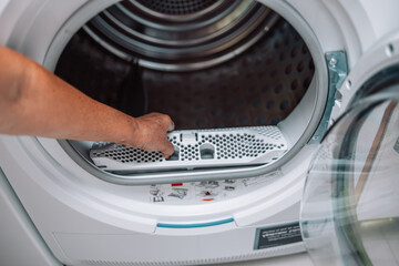 Horizontal photo of female hand taking the lint out from dirty air filter of the dyer machine 