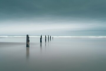  a long exposure photo of a beach with a few posts sticking out of the water in the foreground and a dark sky in the background.  generative ai