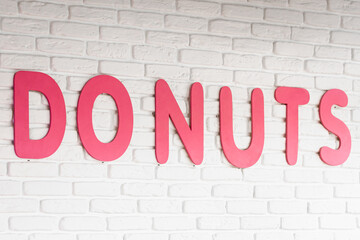The word donuts on a white wall in a cafe, interior decor in a cafe with donuts, close-up lettering.