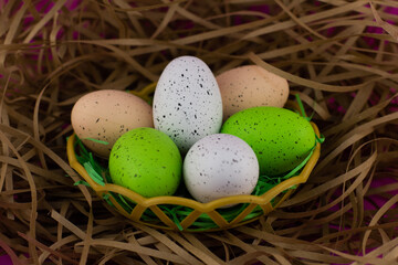 Fototapeta na wymiar In the nest are eggs painted in different colors for the Easter holiday. Chicken eggs prepared for Easter in a wicker bird's nest on a pink background. Easter nest concept with eggs.