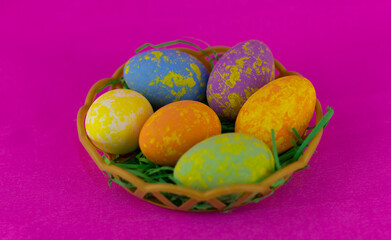 Basket with colorful Easter eggs on a pink background. Beautiful eggs painted in different colors lie in a wicker basket ready for the Easter holiday on a pink background. Easter holiday concept.