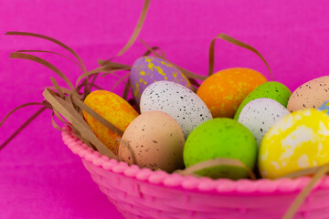 Large basket of colorful Easter eggs on a pink background. Preparation for the bright Christian holiday of Easter. Beautiful bright multi-colored eggs lie in a pink basket on a background isolated.
