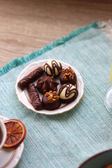 Plate of chocolate pralines, bowl of cookies, cups of tea, glasses of juice and lit candles on the table. Selective focus.