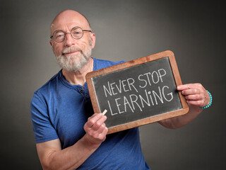 Never stop learning - motivation note on a slate blackboard held by a senior man, teacher, mentor...