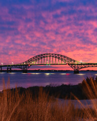 Naklejka premium Vibrant colorful sunset sky behind a long steel tied arch bridge. Fire Island Inlet Bridge, Captree State Park New York
