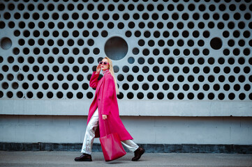 Fashionable confident woman wearing fuchsia color midi coat, sunglasses, metallic pants, combat...