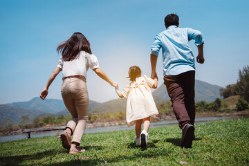 Naklejka na ściany i meble Happy family in the nature travel. family on weekend playing together in the meadow with river Parents hold the child and daughter hands.health life insurance plan concept.