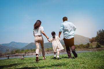 Naklejka na ściany i meble Happy family in the nature travel. family on weekend playing together in the meadow with river Parents hold the child and daughter hands.health life insurance plan concept.