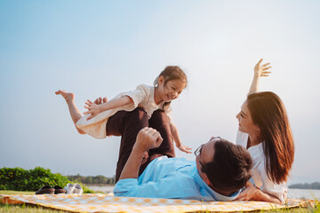 Happy family in the park on weekend. family enjoying together in the meadow with river Parents hold...