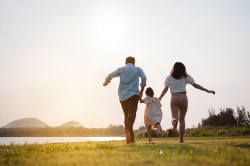 Happy family in the park sunset light. family on weekend running together in the meadow with river...