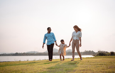 Happy family in the park sunset light. family on weekend running together in the meadow with river Parents hold the child hands.health life insurance plan concept.