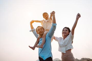 Obraz premium Happy family in the park sunset light. family on weekend running together in the meadow with river Parents hold the child hands.health life insurance plan concept.