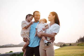 Happy family in the park sunset light. family on weekend playing together in the meadow with river Parents hold the child and daughter hands.health life insurance plan concept.