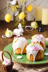 Obraz na płótnie Canvas Mini Easter cakes covered with icing and decorated with sugar flowers on a green plate on a wooden background. Easter table, treats, decor, traditions concept.