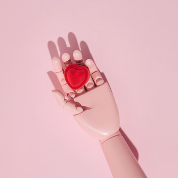 Mannequin hand, pastel pink painted, red heart shape ring box in it, creative love concept, romantic marriage proposal idea.