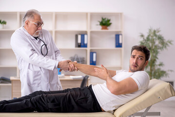 Obraz premium Young male doctor visiting old doctor chiropractor