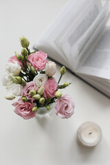 Home decoration and interior. Beautiful burning candle with flowers and book on white table. Details of still life in the home interior of living room. Cozy spring concept. 