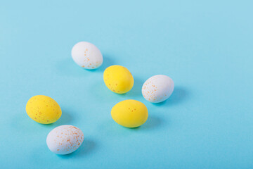 Minimalistic easter background of chocolate candy yellow and white eggs on a blue background