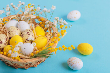 Easter candy chocolate eggs and almond sweets lying in a bird's nest decorated with flowers and feathers on a blue background. Happy Easter concept.