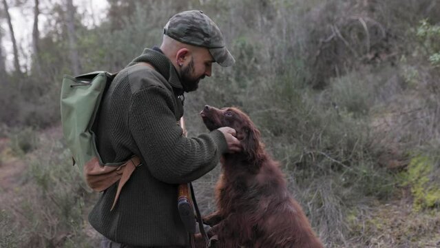 Hunter man with shotgun petting his dogs while hunting together outdoors in nature.