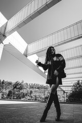 Urban chic: young brunette model wears leather jacket and long boots in public park with morning...