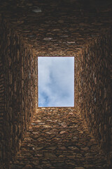 View from the bottom of an old stone light well with a blue sky.