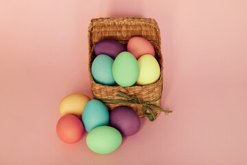 Colored Easter eggs in a square basket on a pink background. Easter